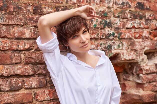 Retro portrait of a stylish beautiful woman in a white shirt against the background of a destroyed building The concept of style and fashion