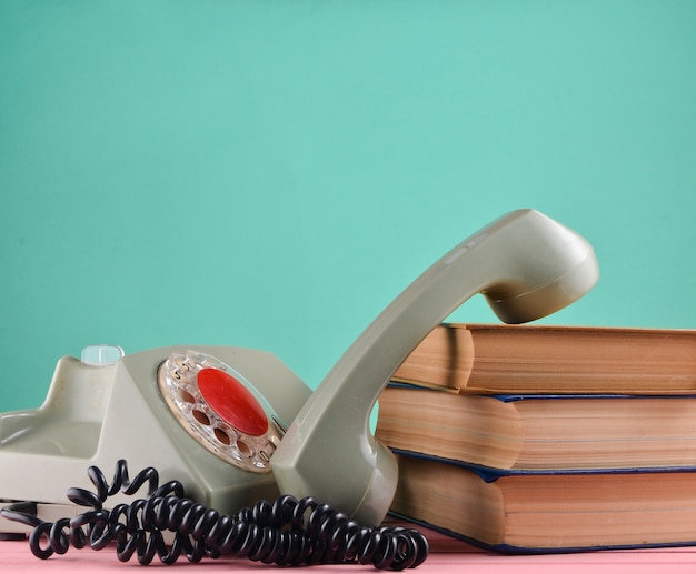 Retro rotary telephone, stack of books on a desk isolated against a green pastel wall