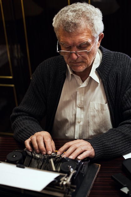 時代遅れのタイプライターにメガネを書いているレトロなシニア男性作家。