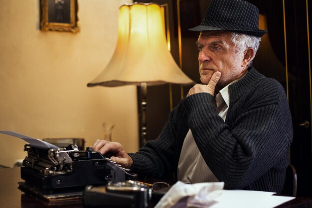 사진 책상에 앉아서 생각하는 모자와 함께 레트로 수석 남자 작가.