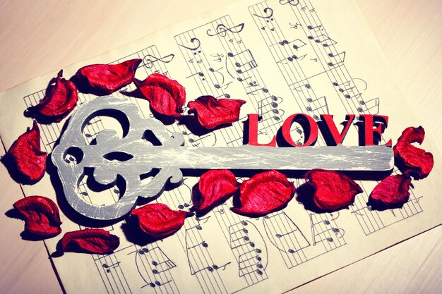 Foto retro sleutel met rozenblaadjes en woord love met papier van muziek op houten tafel achtergrond