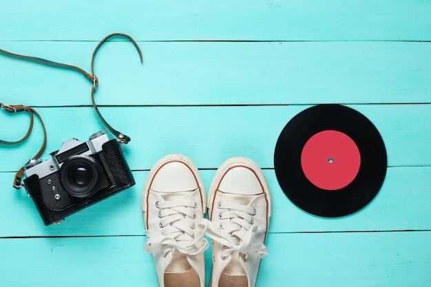 Retro still life. Old fashioned sneakers, vinyl record and vintage film camera on blue wood. Top view. Flat lay