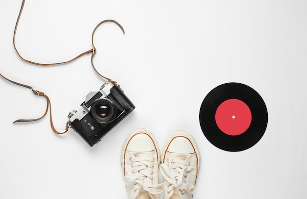 Retro still life. Old fashioned sneakers, vinyl record and vintage film camera on white. Top view. Flat lay