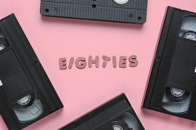 Concetto di stile retrò, anni '80. videocassette su pastello rosa con la parola eighties da lettere in legno