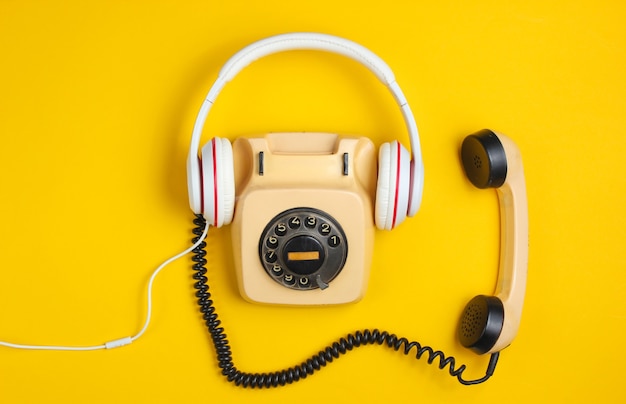 Retro style creative flat lay. Rotary vintage telephone with classic white earphones on a yellow background. Pop culture.