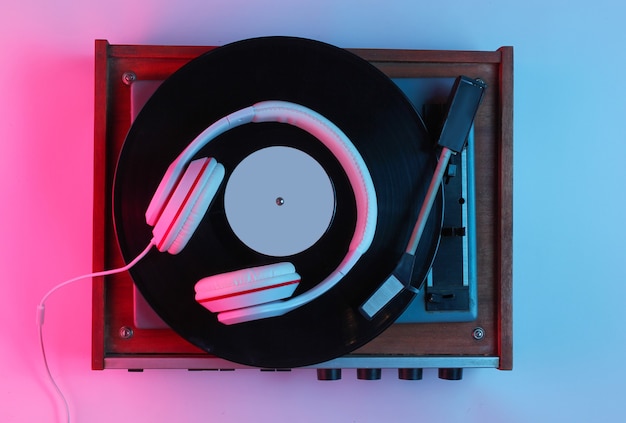 Retro style music concept. Classic headphones, vinyl record player with gradient pink-blue neon light. Pop culture. 80s. Top view