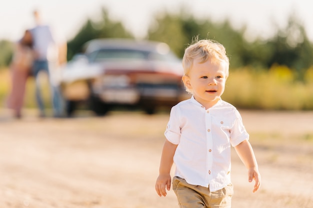 写真 レトロなスタイル。ユニークな車。両親は後ろの車の近くに立っており、息子は前景で彼らから逃げて遊ぶ