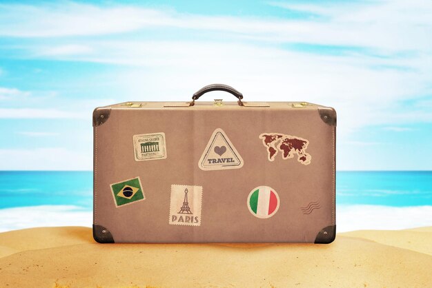 Retro suitcase with travel stickers on beach sand Sea and blue sky in background Summer travel tourism concept