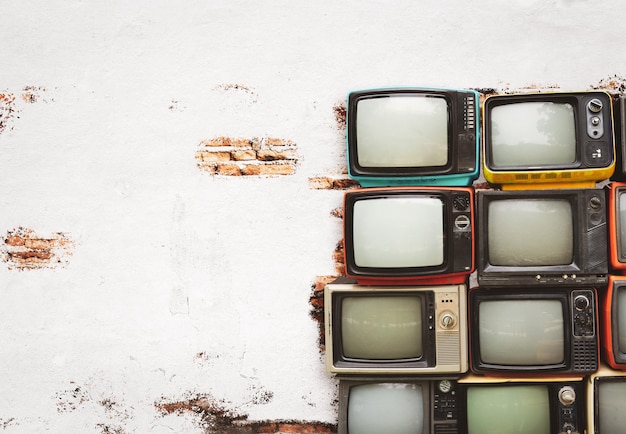 Retro televisions pile on floor in old room with white wall