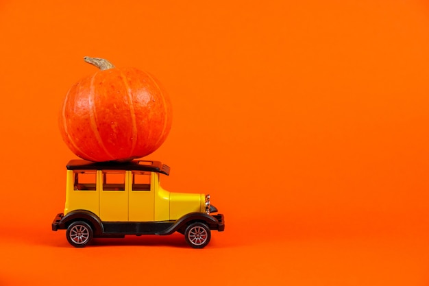 Retro toy car with a pumpkin on an orange background Halloween and autumn harvest concept