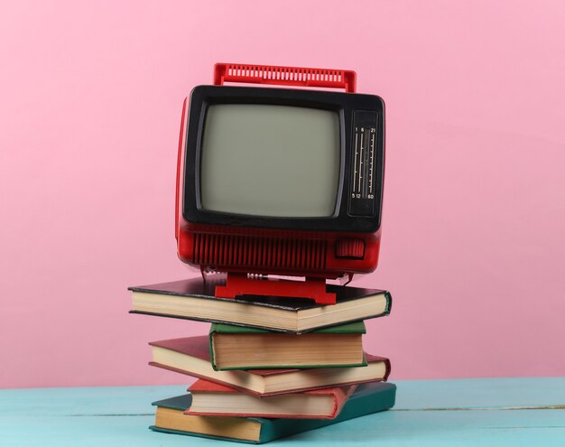 Retro tv en stapel boeken op roze achtergrond. Televisieonderwijs op afstand.