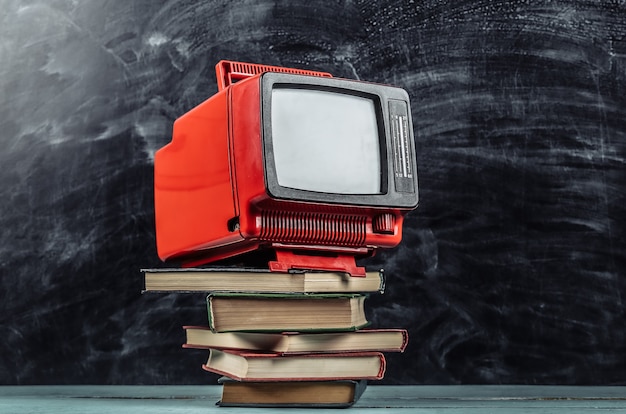 Retro tv and stack of books on blackboard background. TV distance learning.