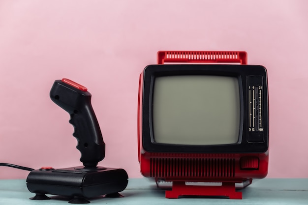 レトロゲーム。ビデオゲームの競争。ピンクの背景にジョイスティックと古いテレビ。属性80年代