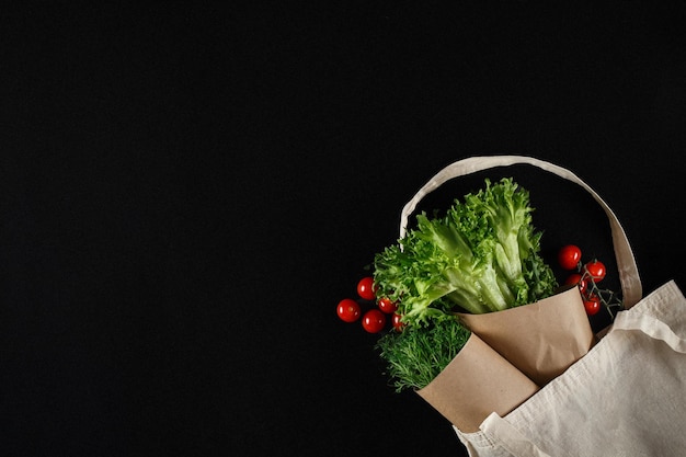 Reusable canvas grocery grocery bag with vegetables and fruits over black background