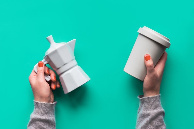 Photo reusable coffee mug or keep cup and white ceramic coffee maker in woman's hands on mint green wall. creative flat lay, top view, trendy zero waste concept, reusable coffee cup with silicone lid.