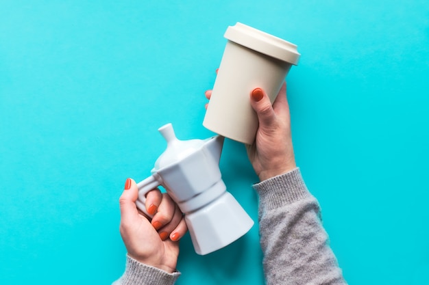 Tazza di caffè riutilizzabile o tenere tazza e caffettiera in ceramica bianca nelle mani della donna sul muro azzurro chiaro. creativo piatto laico, vista dall'alto, concetto zero rifiuti alla moda con tazze di caffè riutilizzabili.