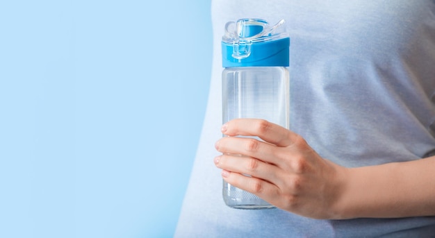 Bottiglia di acqua potabile riutilizzabile per lo sport in mano femminile su backgraund blu. stile di vita sano e concetto di fitness. banner web lungo con spazio di copia.