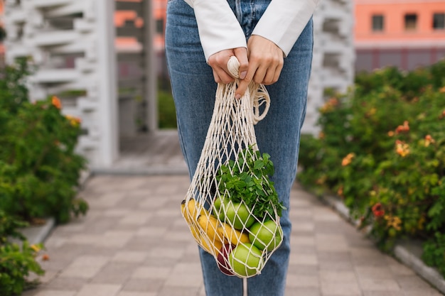 Foto borsa ecologica riutilizzabile per lo shopping. borsa per la spesa in corda con frutta nelle mani di una giovane donna. zero sprechi, concetto plastic free. stile di vita ecologico. acquisto ecologico. consumo consapevole. eco trend.copia spazio