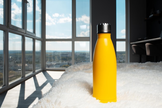 Reusable eco water bottle of yellow color on background of panoramic window