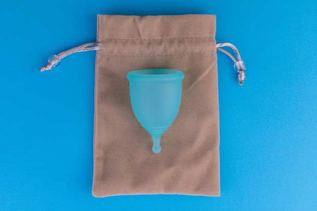 Reusable menstrual cup and eco bag on a blue background Feminine hygiene