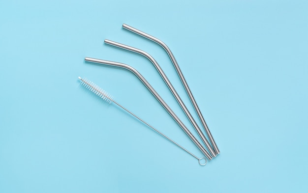 Reusable steel drinking straws and brush on blue background.