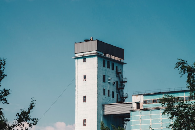 Reusachtige toren van de bouw met meerdere verdiepingen. Pittoreske oude gerenoveerde werkende fabriek. Leeftijd industrieel object. Gevel van grote productie hoogbouw van bomen. Industriegebied close-up.