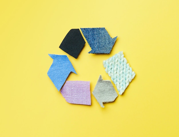 Reuse, reduce, recycle concept background. Recycle symbol made from old clothing on yellow background.