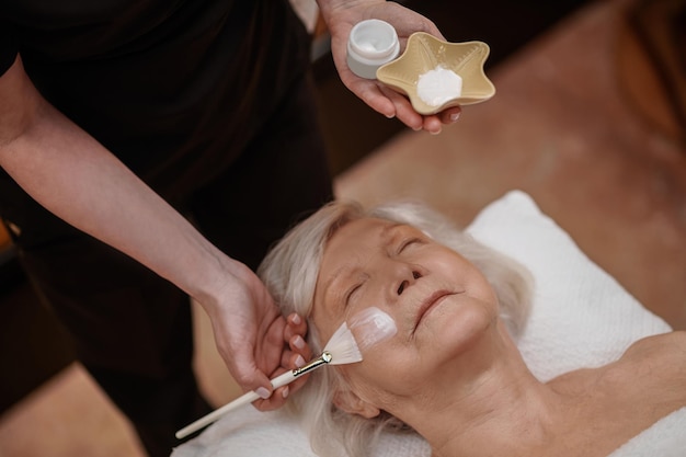 Revitalizing facial mask. Cosmetologist applying facial revitalizing mask on a womans face