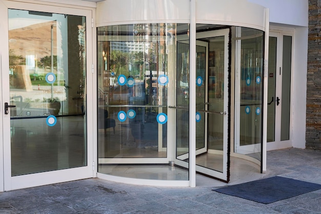 Revolving transparent door to office building entrance sliding
doors front entrance to a hotel in city interior decoration design
cylinder rotate access doorway reflecting buildings in the
glass