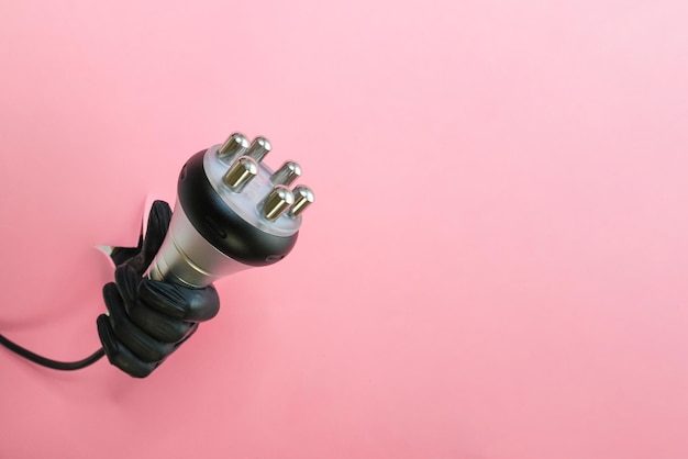 RF lifting hardware massage on a pink background hand in a black glove with an apparatus Cellulite solution and weight loss