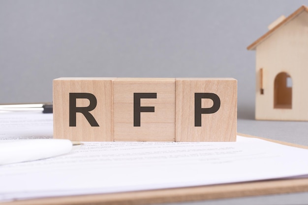 Rfp text made of wooden blocks on gray background with a small wooden model house