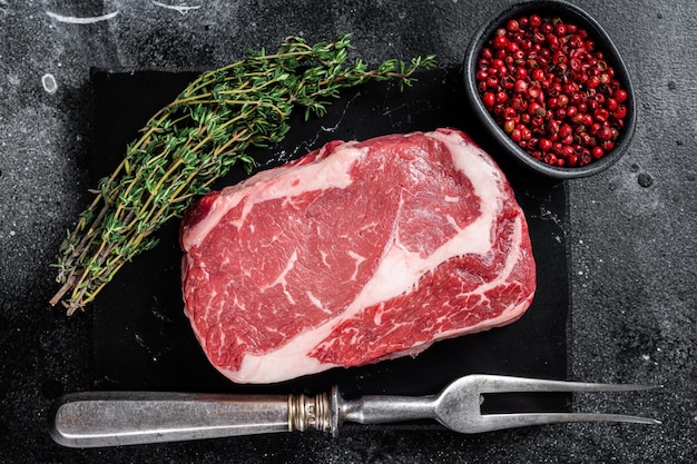 Rib eye ribeye raw Steak beef marbled meat with thyme and pink salt Black background Top view