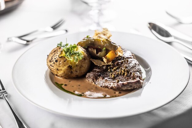 Rib eye steak with brown sauce and whole baked potaties served in a plate