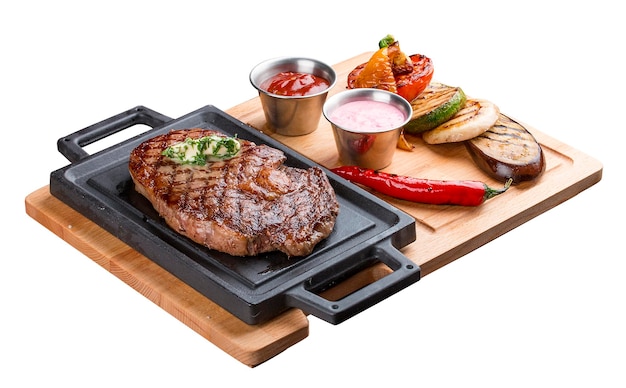 Rib eye steak on wooden tray with grilled vegetables on white background