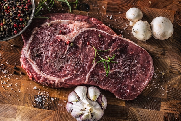 Foto rib eye steak zout peper kruiden knoflook en champignon. rauw rundvlees aan boord van de slager - bovenaanzicht.