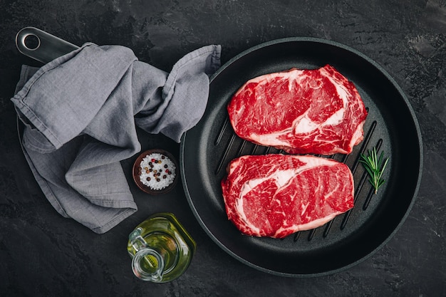 Ribeye 스테이크 원시 신선한 쇠고기 고기와 소금과 로즈마리를 어두운 석재 배경의 그릴 팬에