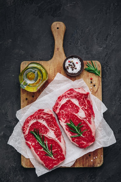 Ribeye Steak Raw fresh beef meat with salt and rosemary ready for barbecue on dark stone background