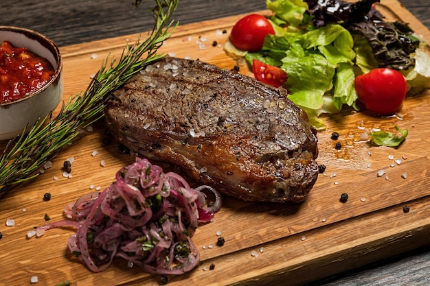 Ribeye steak served on a wooden board with sauce fresh vegetables pickled onions and rosemary Restaurant menu closeup shot