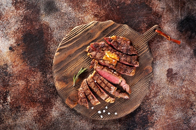 Ribeye steak slices on a wooden serving board on a concrete background