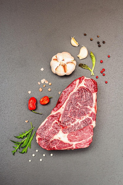 Ribeye steak with spices and herbs on black stone background