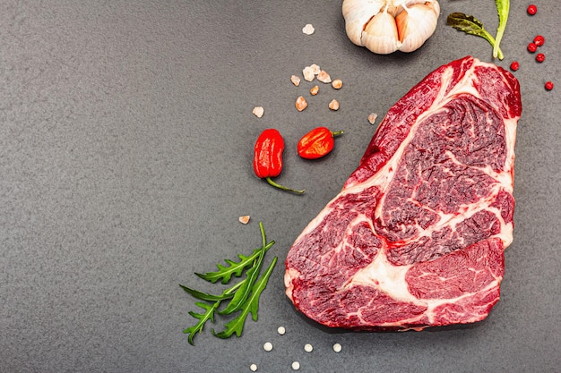 Ribeye steak with spices and herbs on black stone background