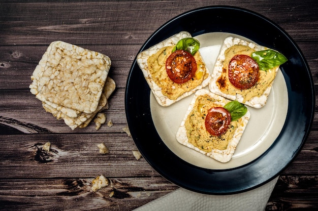 Cracker di riso con hummus di ceci pomodorini e basilico fresco su un piatto e cracker su un tavolo rustico