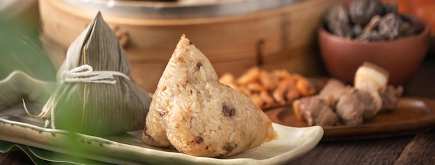 Rice dumpling chinese zongzi food in a steamer on wooden table\
with red brick wall window background at home for dragon boat\
festival concept close up