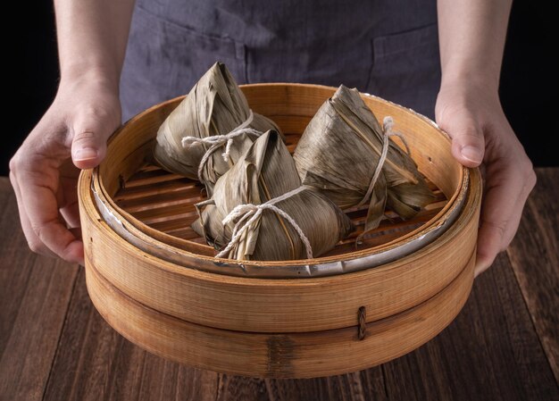 Rice dumpling zongzi bunch of chinese traditional cooked food
on wooden table over black background concept of dragon boat
festival close up copy space