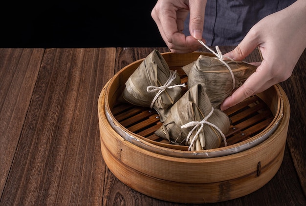 Rice dumpling zongzi bunch of chinese traditional cooked food\
on wooden table over black background concept of dragon boat\
festival close up copy space