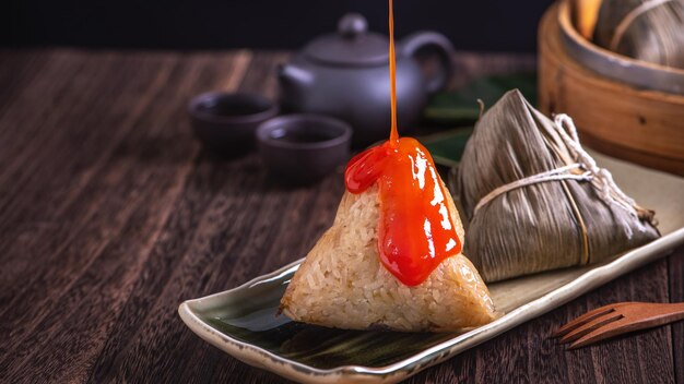 Rice dumpling zongzi bunch of chinese traditional cooked food\
on wooden table over black background concept of dragon boat\
festival close up copy space