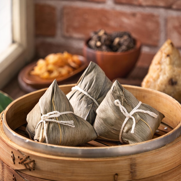 만두 zongzi 중국식 만두 zongzi는 드래곤 보트 페스티벌(Dragon Boat Festival) 컨셉을 위해 집에서 붉은 벽돌 창문 배경이 있는 나무 탁자 위의 증기선에 있습니다.