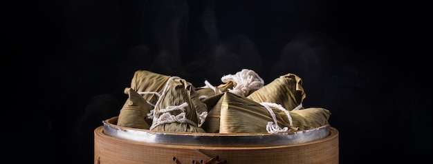 Rice dumpling zongzi dragon boat festival bunch of chinese\
traditional cooked food in steamer on wooden table over black\
background close up copy space