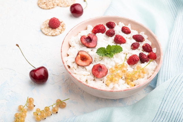 Porridge di fiocchi di riso con latte e fragole in una ciotola di ceramica su una superficie di cemento bianco e tessuto di lino blu