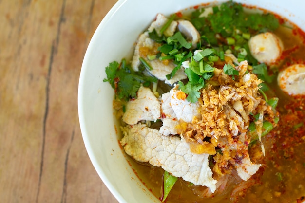 Rice noodle in spicy soup with pork ball, vegetable and pork serving on wooden desk in canteen